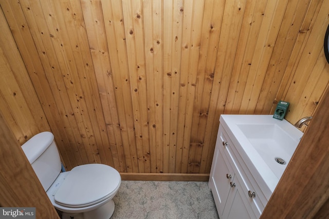 half bath with vanity, toilet, baseboards, and wood walls