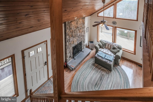 living area featuring high vaulted ceiling, a ceiling fan, wood finished floors, a stone fireplace, and wood ceiling