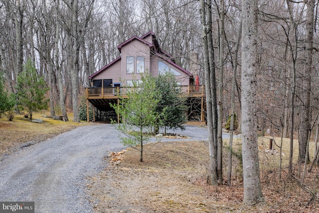 rustic home with a carport, a wooden deck, a forest view, and dirt driveway