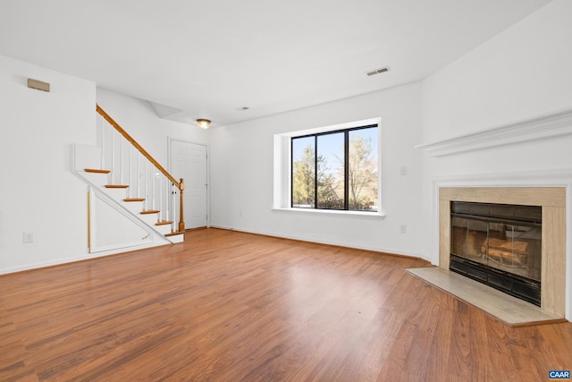 unfurnished living room with stairs, baseboards, wood finished floors, and a glass covered fireplace