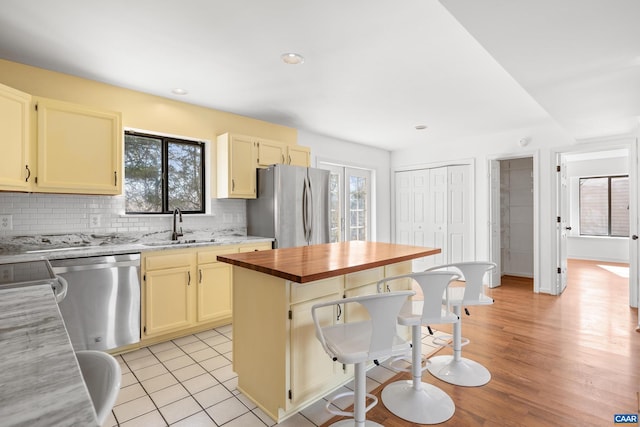 kitchen with a breakfast bar, a sink, appliances with stainless steel finishes, backsplash, and a center island