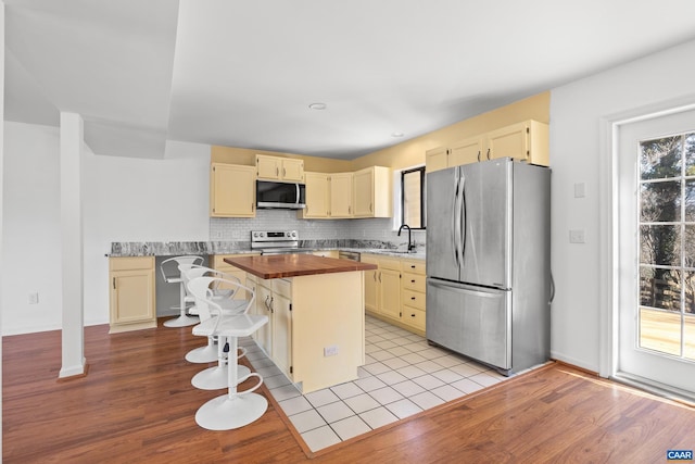 kitchen with stainless steel appliances, tasteful backsplash, wooden counters, light wood-style flooring, and a sink