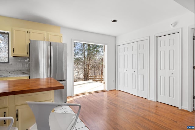 kitchen with light wood-style flooring, wood counters, baseboards, freestanding refrigerator, and decorative backsplash