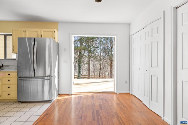 kitchen with light wood finished floors, baseboards, decorative backsplash, freestanding refrigerator, and light countertops