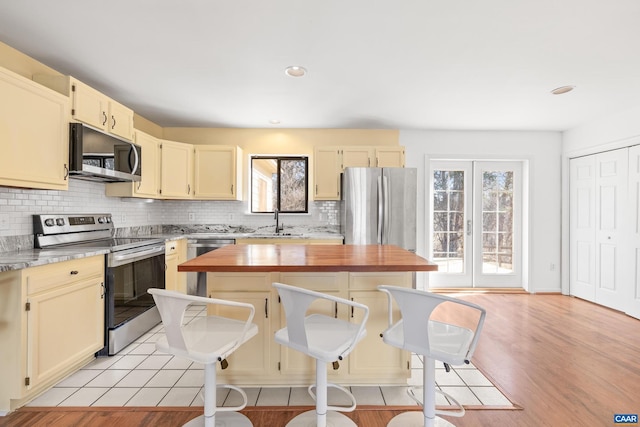 kitchen featuring stainless steel appliances, a sink, wood counters, a center island, and tasteful backsplash