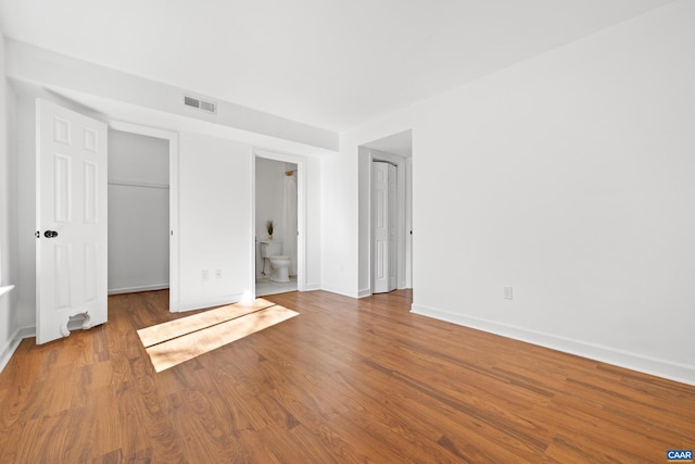 unfurnished bedroom featuring a walk in closet, visible vents, baseboards, and wood finished floors