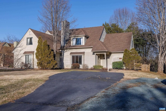 cape cod house with a shingled roof, a chimney, and aphalt driveway