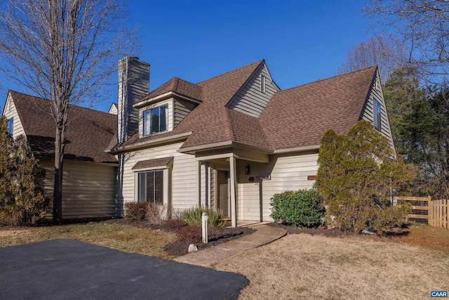 view of front facade with roof with shingles, a chimney, and fence