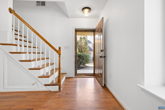 foyer featuring baseboards, stairs, visible vents, and wood finished floors