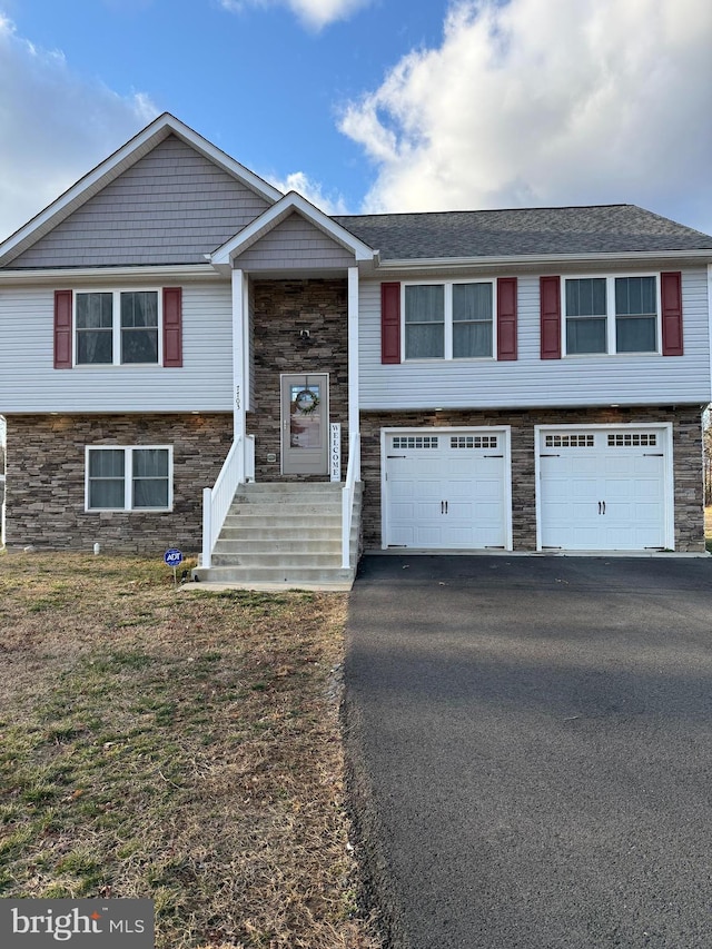 raised ranch featuring a garage, stone siding, and aphalt driveway