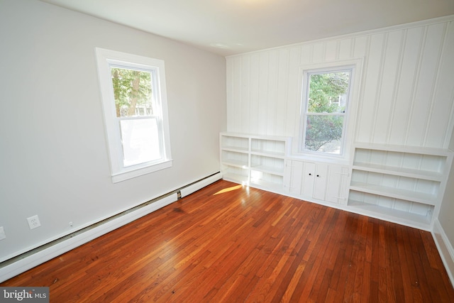 spare room with built in features, wood-type flooring, a healthy amount of sunlight, and baseboard heating