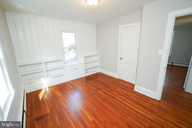 spare room with hardwood / wood-style flooring, baseboards, built in shelves, and a baseboard heating unit