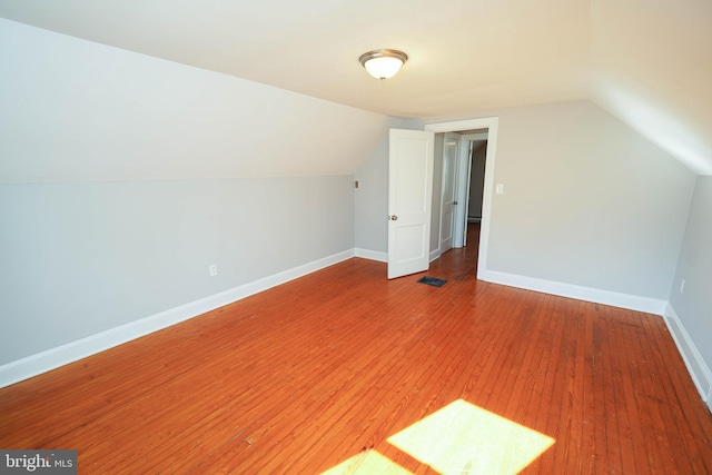 additional living space featuring baseboards, vaulted ceiling, visible vents, and light wood-style floors