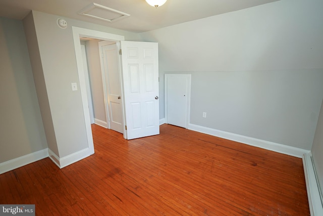 unfurnished bedroom featuring attic access, baseboards, and wood finished floors