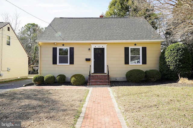 bungalow featuring entry steps, a shingled roof, and a front lawn