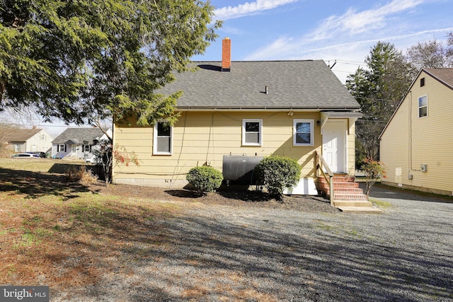 rear view of property featuring a shingled roof, entry steps, a chimney, and heating fuel