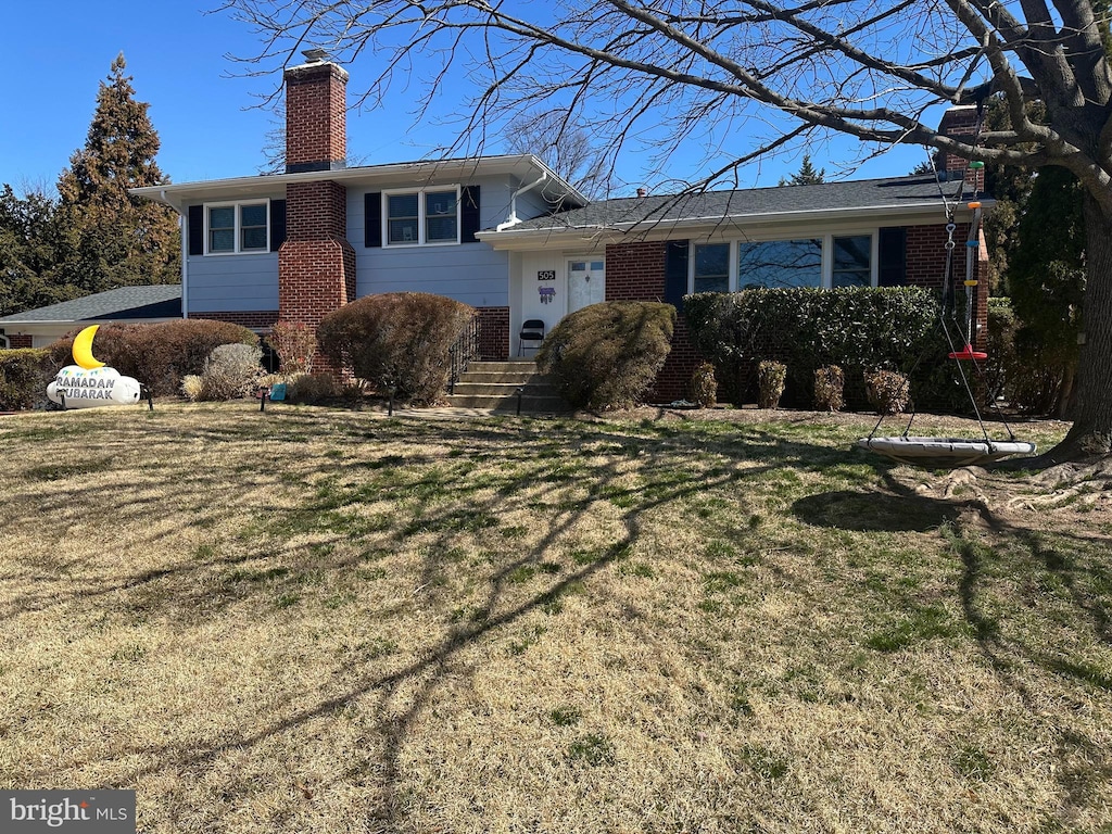 tri-level home featuring brick siding, a chimney, and a front yard