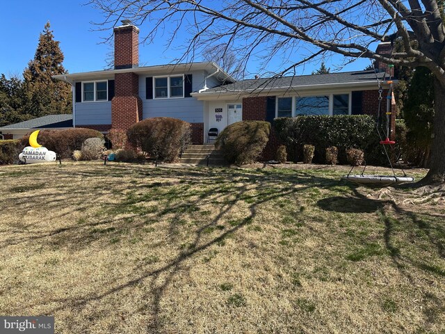 tri-level home featuring brick siding, a chimney, and a front yard