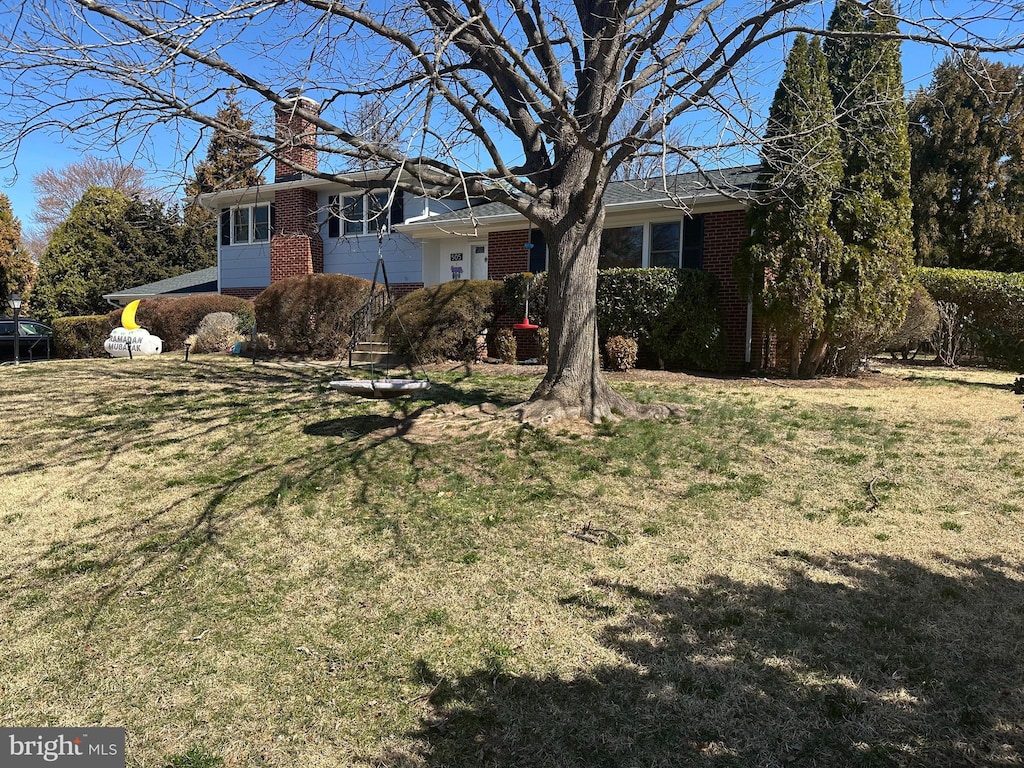 view of front of house with brick siding, a chimney, and a front lawn