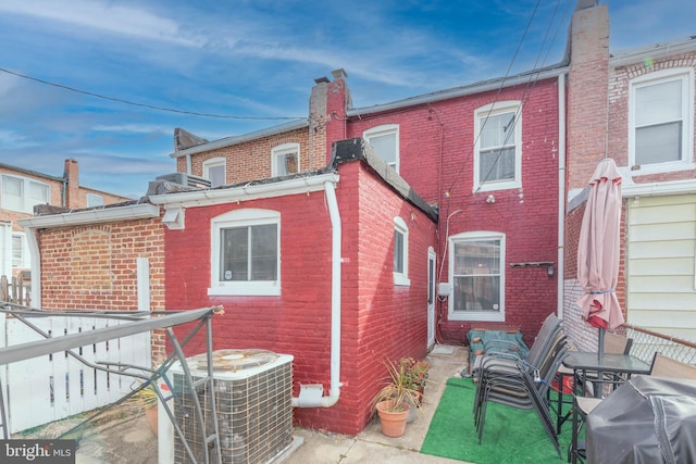 back of house featuring a chimney, cooling unit, and brick siding