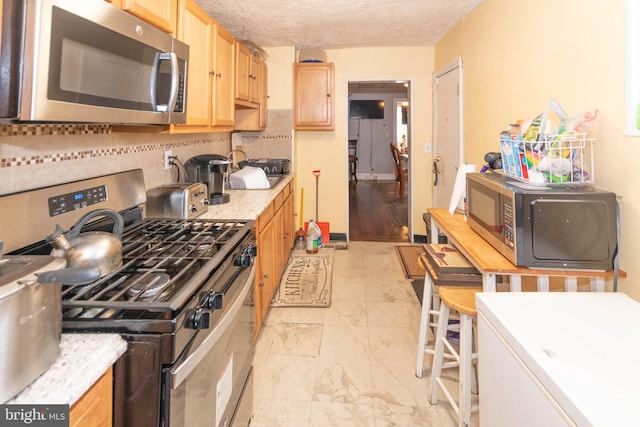 kitchen with stainless steel appliances, tasteful backsplash, light brown cabinets, and light countertops