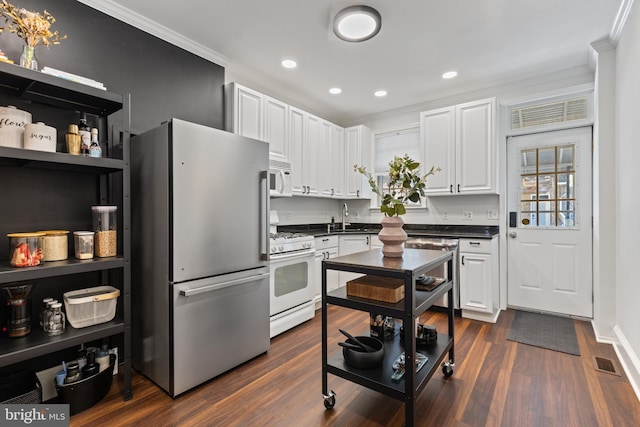 kitchen with white appliances, dark countertops, dark wood-type flooring, crown molding, and a sink