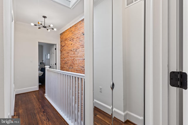 corridor with baseboards, hardwood / wood-style flooring, brick wall, ornamental molding, and a chandelier