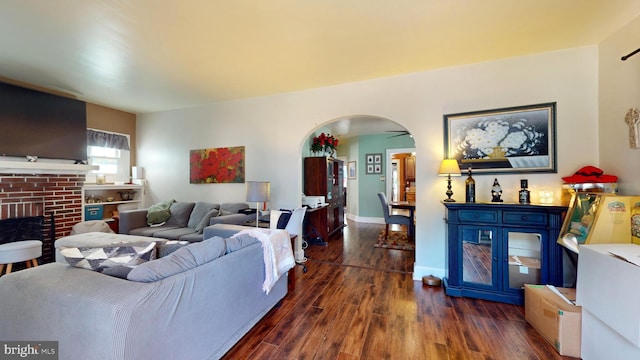 living area featuring dark wood-style floors, baseboards, a fireplace, and arched walkways