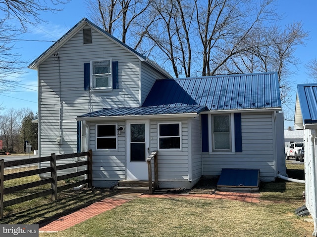 rear view of property featuring entry steps, fence, metal roof, and a lawn