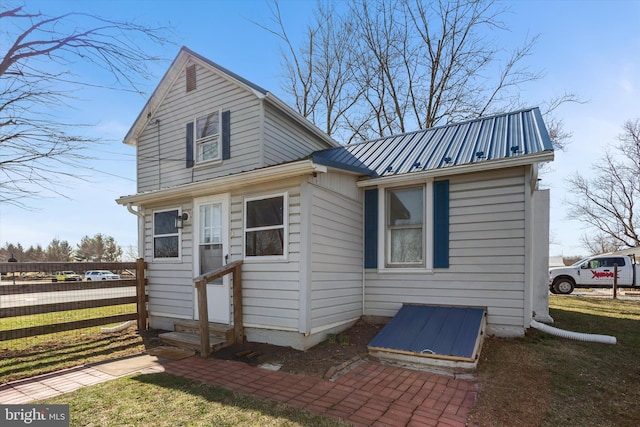 view of front of home with entry steps, metal roof, a front lawn, and fence