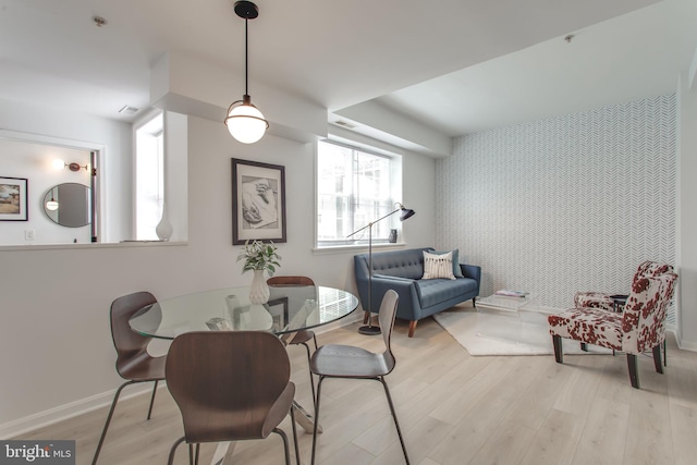 dining room featuring light wood finished floors, visible vents, an accent wall, baseboards, and wallpapered walls