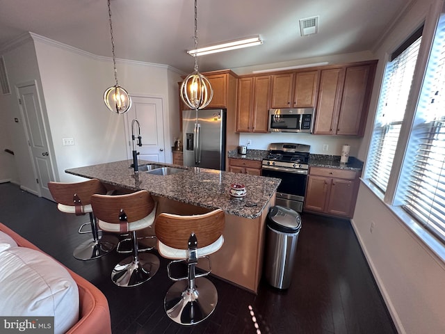 kitchen with dark wood-type flooring, a kitchen island with sink, ornamental molding, a sink, and stainless steel appliances