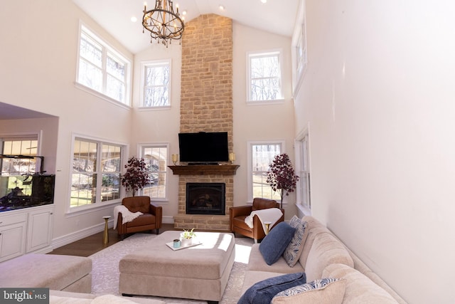 living room featuring a stone fireplace, plenty of natural light, an inviting chandelier, and wood finished floors