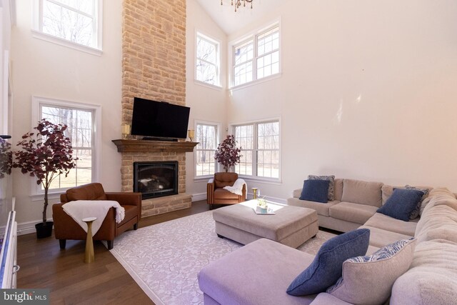 living room with a stone fireplace, wood finished floors, baseboards, and high vaulted ceiling