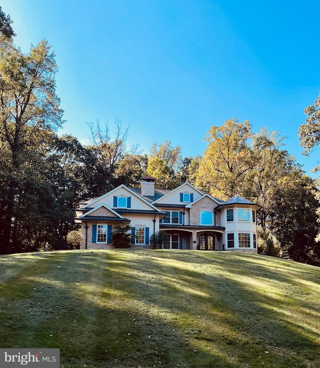 view of front facade featuring a front lawn, stone siding, and a chimney