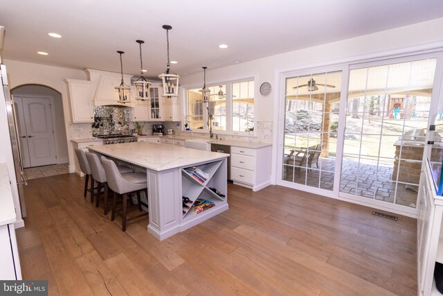 kitchen with decorative backsplash, glass insert cabinets, light wood-style floors, white cabinetry, and a center island