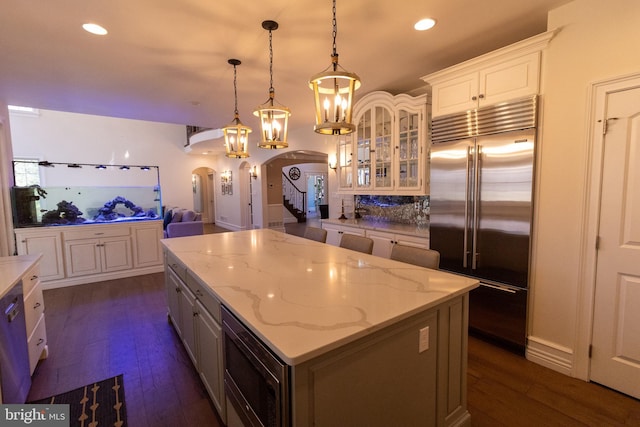 kitchen with a center island, glass insert cabinets, dark wood-type flooring, built in appliances, and arched walkways