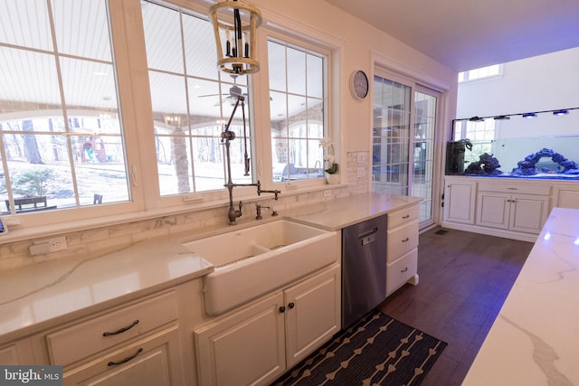 kitchen featuring dark wood-type flooring, light stone counters, stainless steel dishwasher, white cabinetry, and a sink