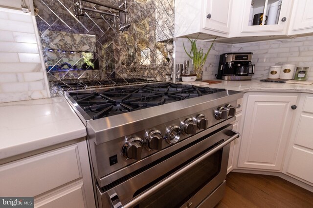 kitchen with backsplash, light stone countertops, high end stove, and white cabinetry