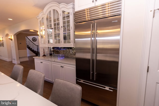 kitchen featuring white cabinetry, glass insert cabinets, arched walkways, and built in fridge