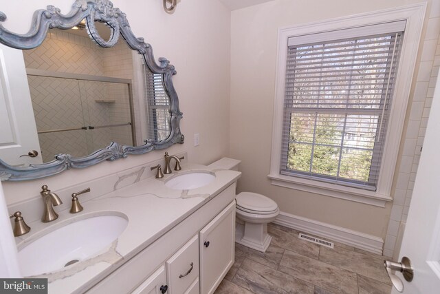 full bathroom with a shower with door, visible vents, double vanity, and a sink