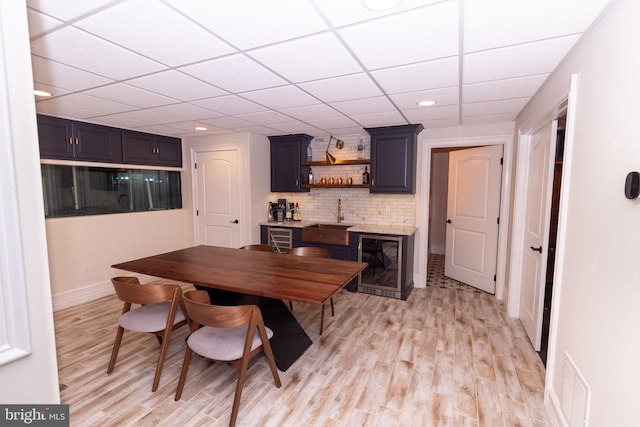 dining room featuring indoor wet bar, a paneled ceiling, baseboards, and light wood finished floors