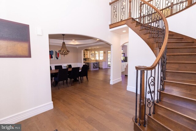 stairway featuring crown molding, baseboards, wood finished floors, arched walkways, and a raised ceiling