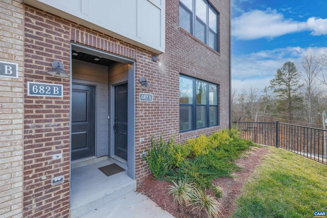 doorway to property featuring fence and brick siding