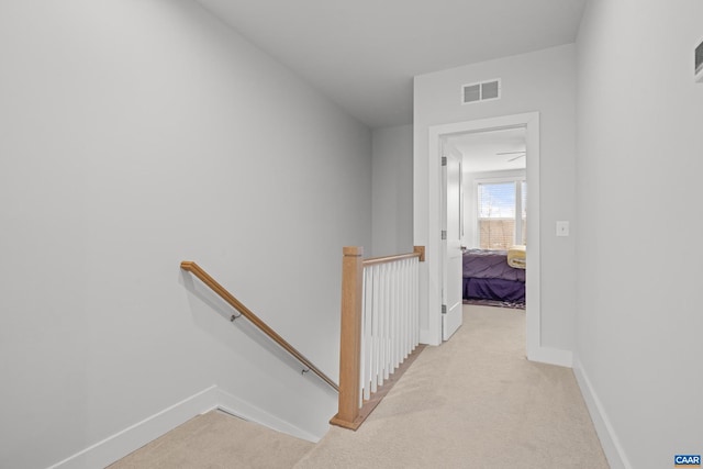 corridor with light carpet, visible vents, an upstairs landing, and baseboards