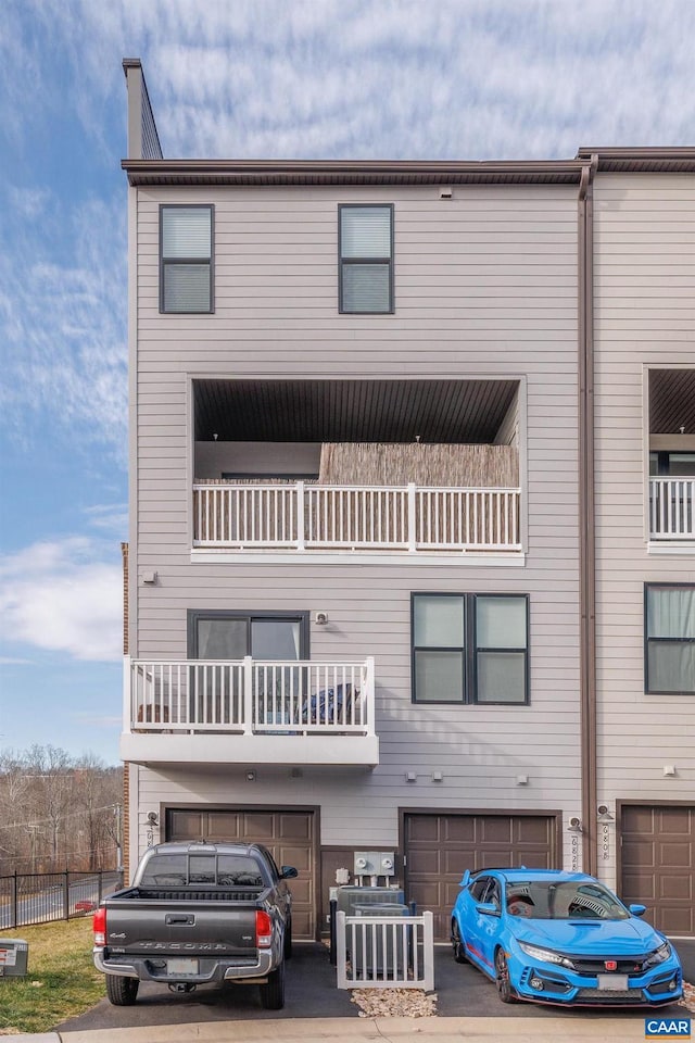 view of front facade with driveway, a balcony, a garage, and fence