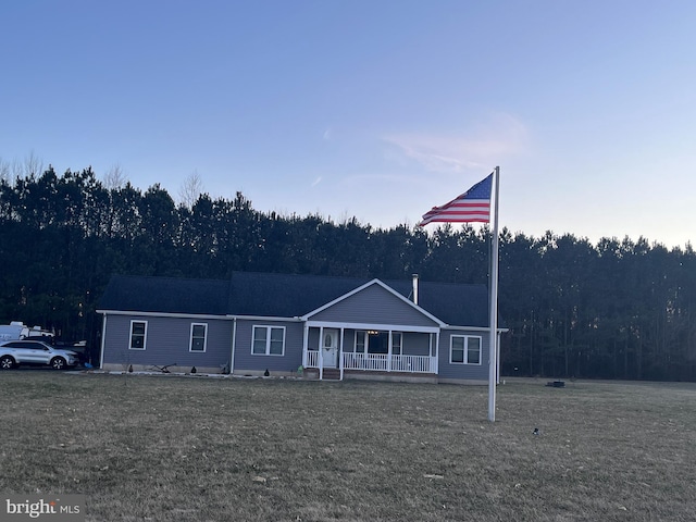 view of front facade with a forest view, a front lawn, and a porch