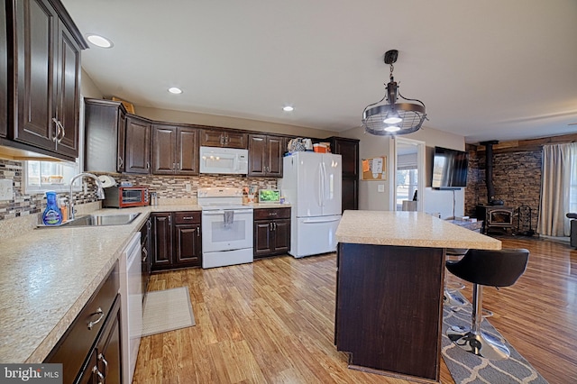 kitchen featuring light countertops, open floor plan, a sink, dark brown cabinets, and white appliances