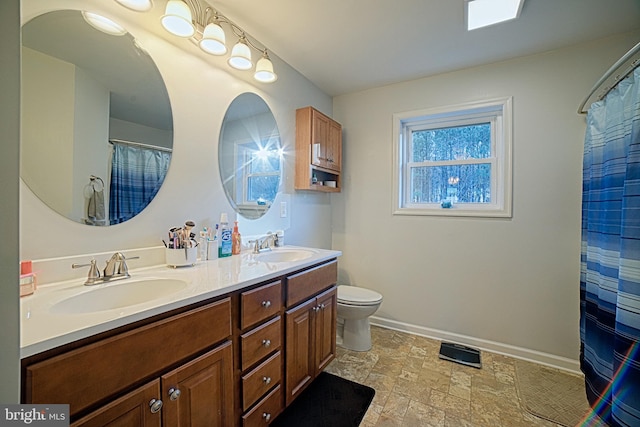 bathroom with stone finish floor, a sink, baseboards, and double vanity