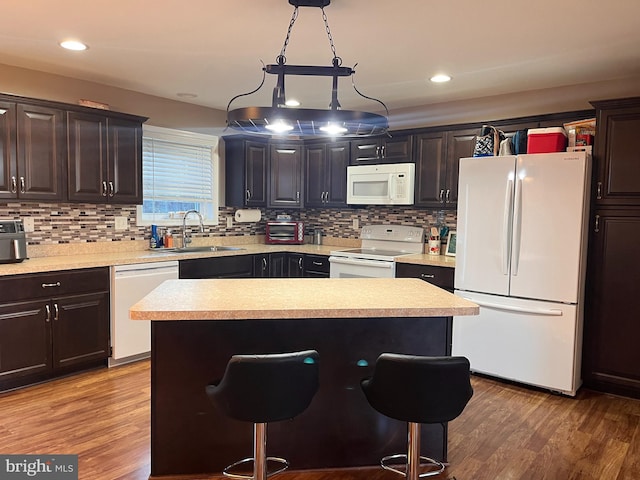 kitchen with light countertops, a sink, wood finished floors, white appliances, and a kitchen breakfast bar